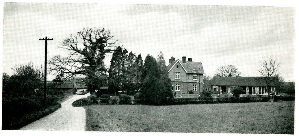 A black and white photo of Dedisham School just off a countryside road and fields.
